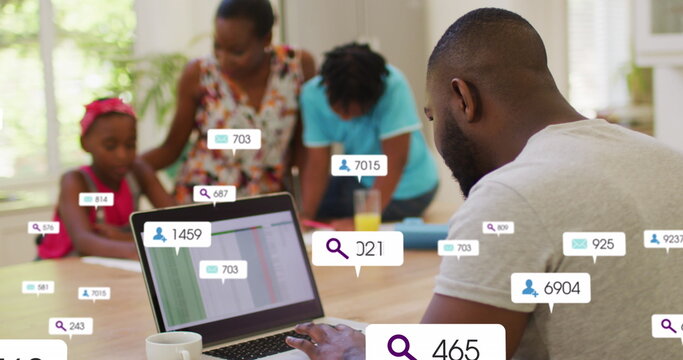 African american businessman using laptop while family in background, icons of increasing followers - Powered by Adobe