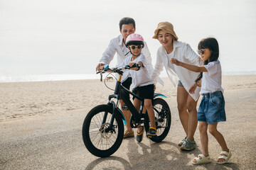 Family fun under summer sun: Parents happily teach their children to ride bicycles on sandy beach...