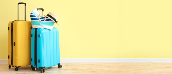 Packed suitcases with beach bag and hat near color wall