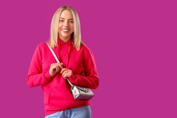 Beautiful young woman in stylish hoodie with bag on purple background