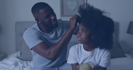 African American father/older brother, tying hair of young daughter on bed
