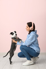 Beautiful young woman in headphones playing with cute staffordshire terrier puppy on floor near...