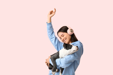 Beautiful young woman in headphones with cute staffordshire terrier puppy listening music on pink...