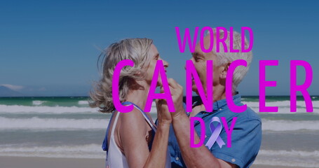 Fototapeta premium Image of world cancer day over happy caucasian senior couple dancing on beach