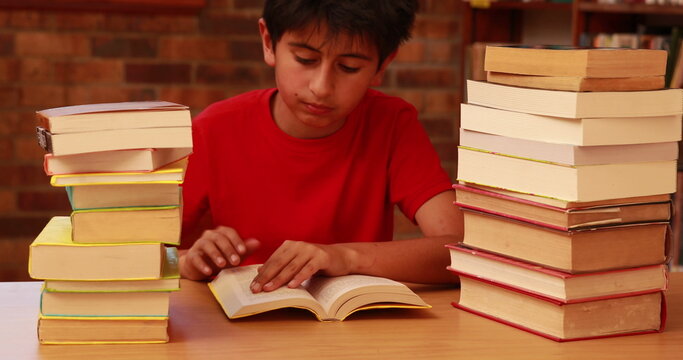Boy in red shirt reading between stacks of books, focusing intently on text - Powered by Adobe