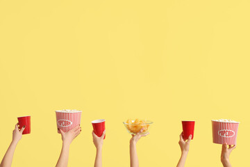 Hands holding buckets with popcorn, drinks and potato chips on yellow background