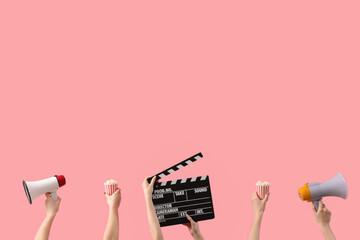 Hands holding buckets with popcorn, movie clapper and megaphones on pink background