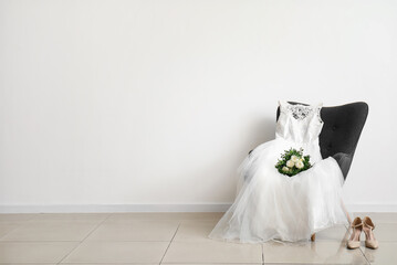 Wedding dress, bridal bouquet on grey chair and wedding shoes on floor in room