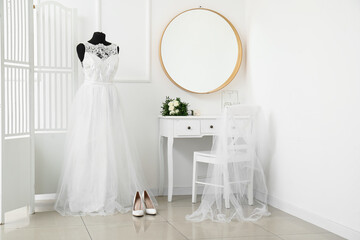 Mannequin with wedding dress and wedding bouquet on white dressing table in light room