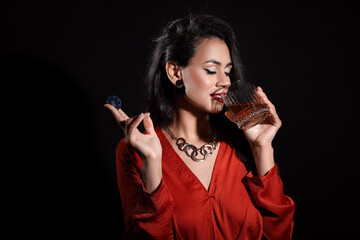 Beautiful young African-American woman with glass of whiskey and poker chip on black background