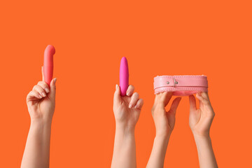 Female hands with vibrators and collar from sex shop on orange background, closeup