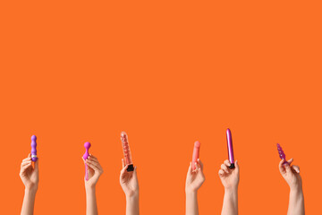 Female hands with different sex toys on orange background