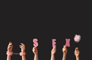 Female hands with word SEX, feather stick and handcuffs on dark background