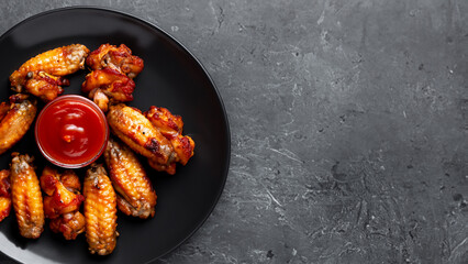 Grilled spicy chicken wings with ketchup on a black plate on a dark slate, stone. Generative Ai
