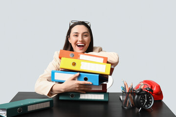 Happy businesswoman with folders sitting at table on light background