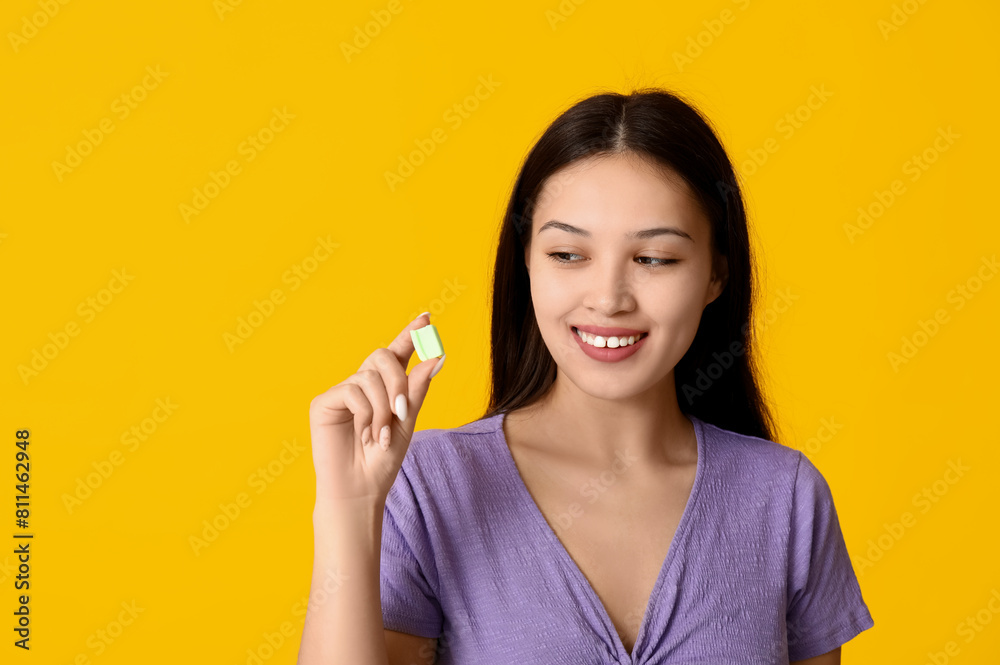 Sticker Beautiful young Asian woman with chewing gum on yellow background