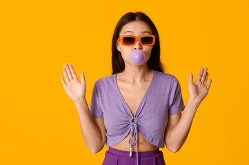 Beautiful surprised Asian woman with chewing gum on yellow background