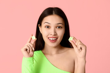 Beautiful surprised Asian woman with chewing gums on pink background