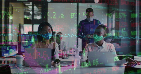 Image of trading board and graph on diverse coworkers wearing mask talking and working on laptop