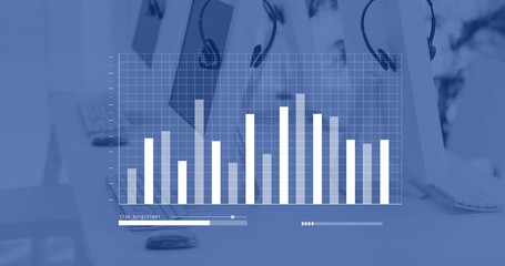 Blue and white graph processing data over computers and phone headsets on desks in empty office