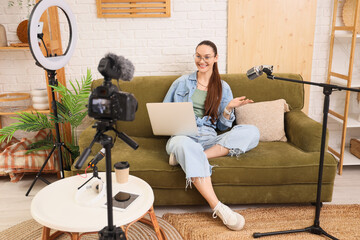 Young woman with laptop on sofa recording podcast in studio