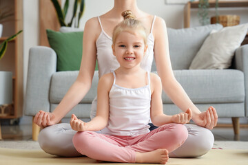 Sporty mother with her little daughter meditating in living room