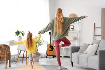 Beautiful young sporty woman with her little daughter practising yoga in living room