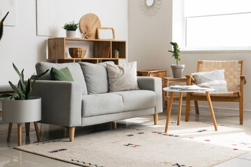 Interior of cozy living room with sofa, shelving unit and houseplants near white wall