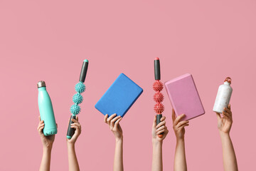Female hands with yoga blocks, sports water bottles and roller massager sticks on pink background