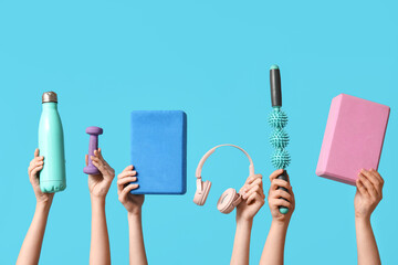Female hands with yoga blocks, sports water bottle, roller massager stick, dumbbell and headphones...