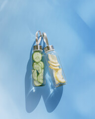 Top view two glass bottles, water drink detox with lemon and cucumber at sunlight on blue...