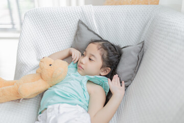 cute asian children stretching on white sofa, she sleepy and lazy in the morning, she hug a bear doll, child health promotion