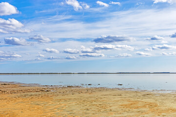 Scenic summer landscape blue sky clouds, water surface and sandy shore. Minimal aesthetic nature view. Pastel colors cloudscape. Ulzhay (Uldjay) salt lake with medicinal mud in Omsk region