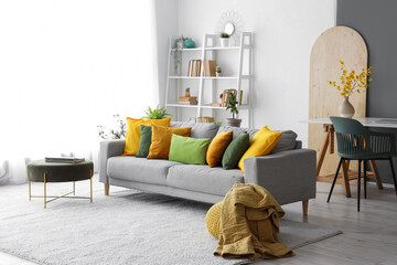 Interior of stylish living room with plants, workplace and colorful pillows on sofa