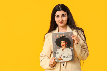 Beautiful young happy woman with magazine on yellow background
