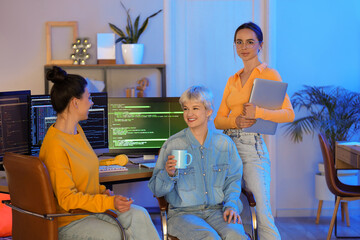 Team of female programmers with coffee and laptop working in office at night