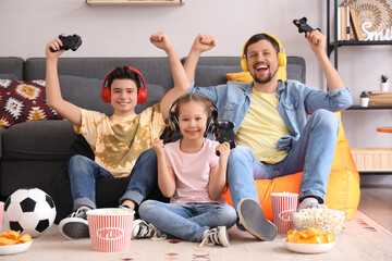 Happy father with his little children in headphones playing video game on beanbags at home