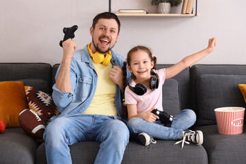 Happy father with his little daughter playing video game on sofa at home
