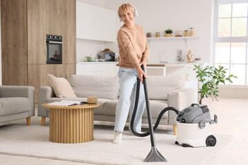 Mature woman in headphones cleaning carpet at home