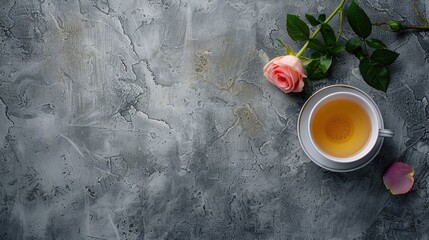 Top down view of a cup of tea adorned with a delicate pink rose set against a backdrop of grey stone with ample space for text or design elements