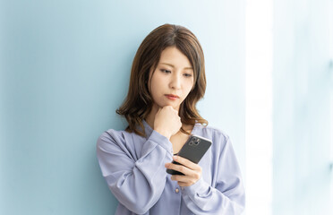 スマートフォンを見て真剣な表情で考える日本人女性