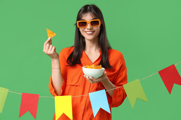 Young woman with nachos and colorful bunting on green background. Cinco de Mayo celebration