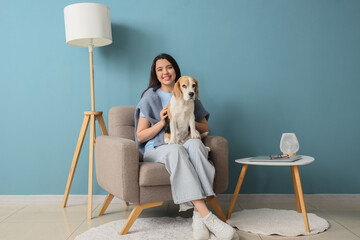 Young woman with cute dog sitting in grey armchair near blue wall at home