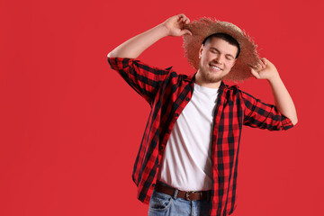Happy young man with straw hat on red background. Festa Junina celebration