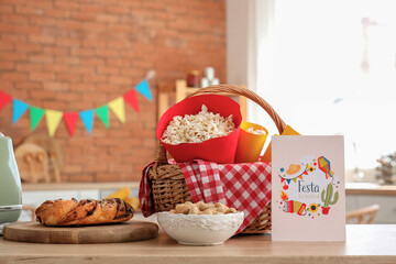 Wicket basket with popcorn, peanuts and greeting card on table in kitchen. Festa Junina celebration