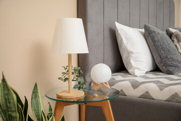 Bedside table with lamp near cozy bed in bedroom