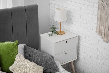 Bedside table with lamp near cozy bed in bedroom