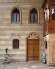 A Mamluk style stone facade featuring a richly decorated wooden door, Gothic-style windows, and an intricate wooden balcony