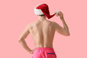 Young man in Santa hat with sun made of sunscreen cream on pink background, back view. Christmas in...