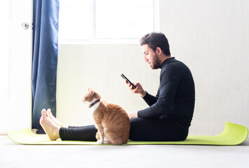 Joven apuesto usando su teléfono celular a lado de su gato. Hombre y su mascota 